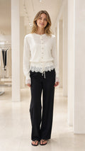 Front view of White lace-trimmed knit cardigan paired with black trousers