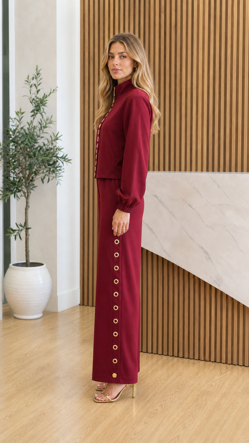 Side profile view of model in burgundy pants set showing side gold eyelet details