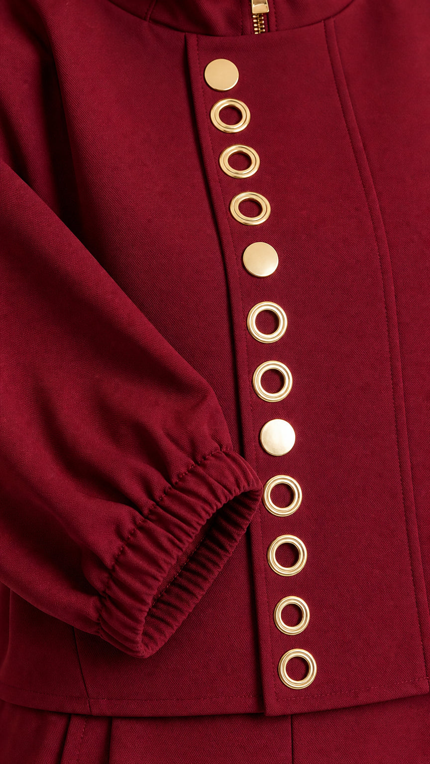 Close-up detail of gold-tone button and eyelet trim on burgundy top and sleeve cuff